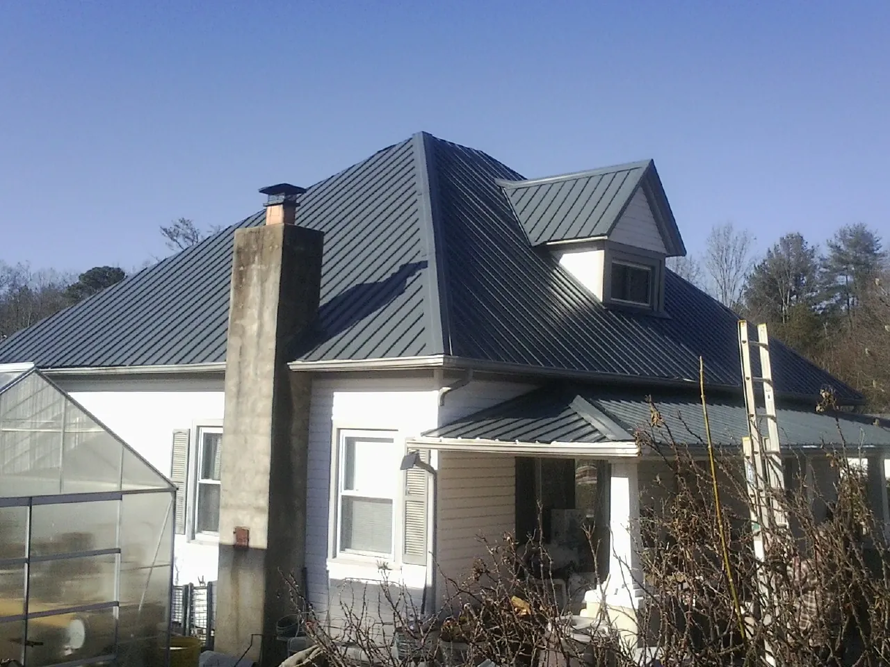 Dark blue standing seam metal roof on a white farmhouse with dormer — Slate & Tile Roof Repair by Roofing Brothers in Fairhaven