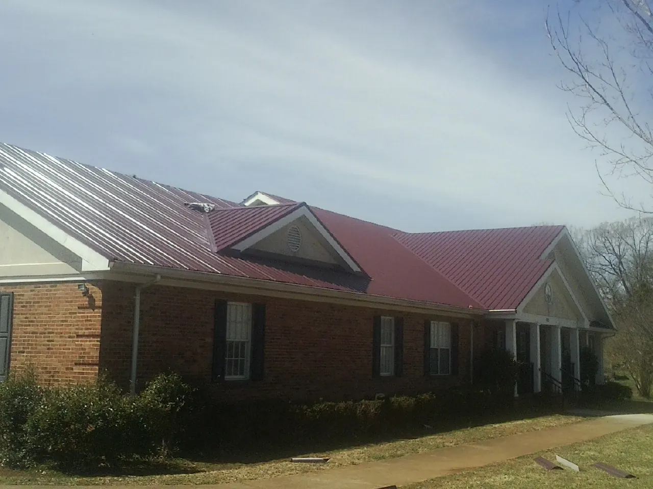 Red metal roof with gabled entries on a long brick building, from a Hail Damage Roof Repair job in Fairhaven