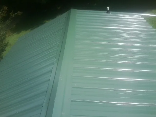 New green metal panels meeting at the ridge of a roof — Flat Roof Repair work by our crew in Fairhaven