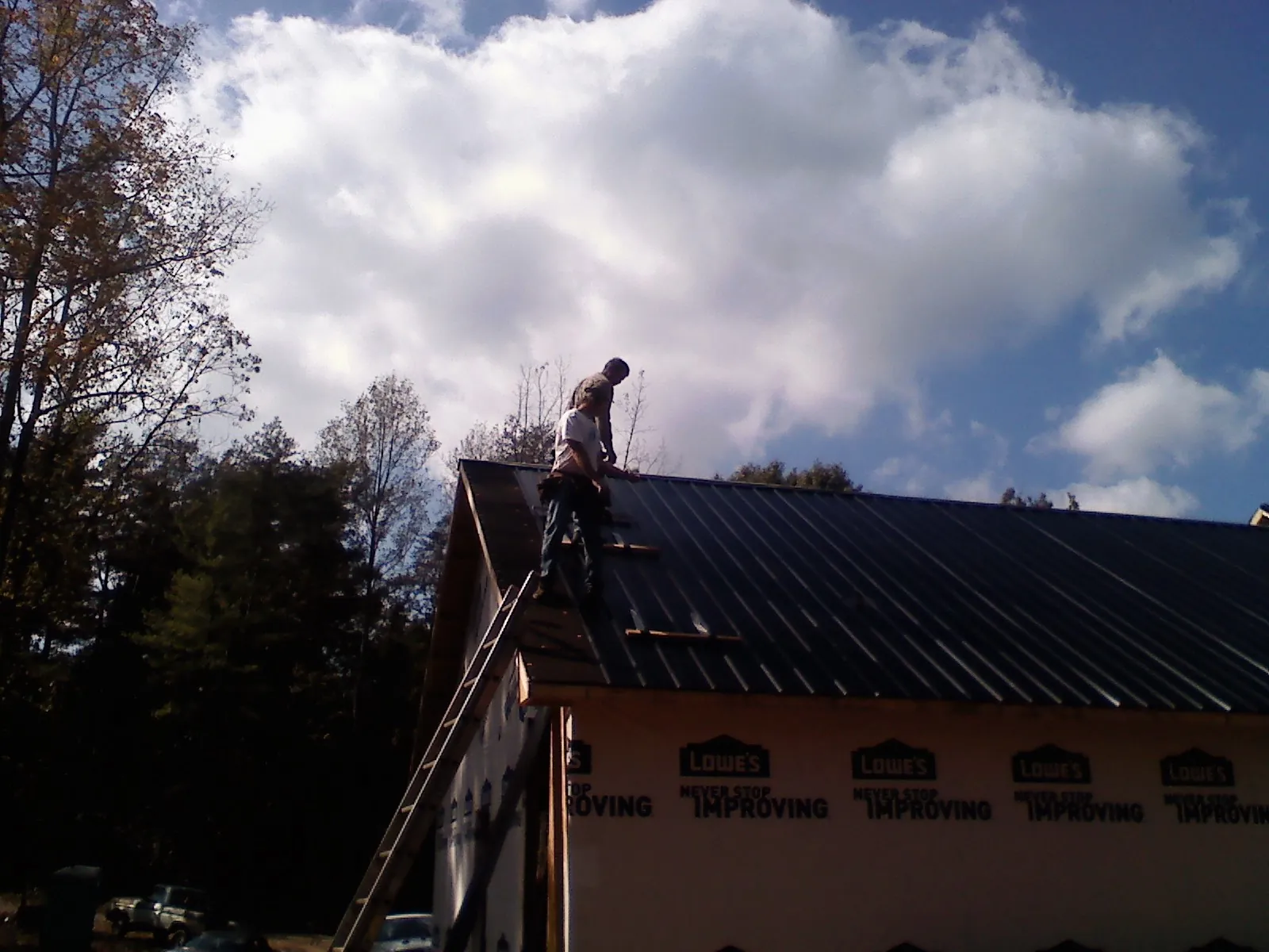 Roofer fastening dark metal panels high against a cloudy sky, from a Roof Inspection job in Fairhaven