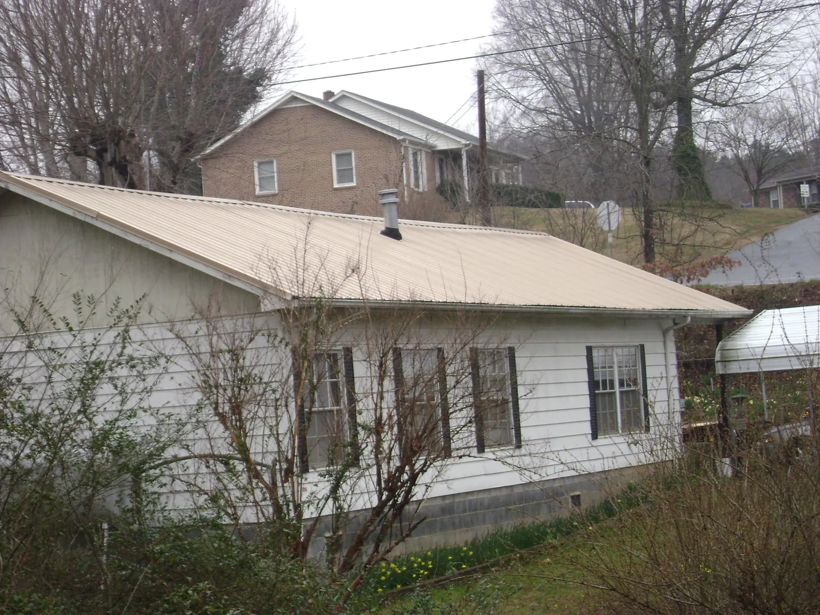 Tan metal roof on a white sided house set into a hillside — Commercial Roofing by Roofing Brothers in Fairhaven